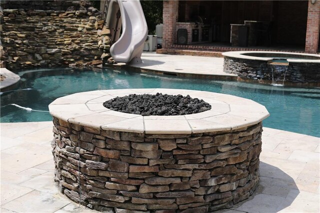 view of swimming pool with pool water feature, an outdoor fire pit, an in ground hot tub, and a water slide