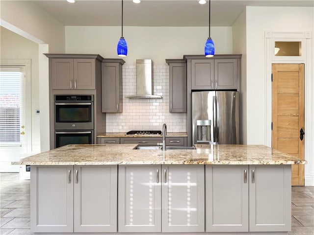 kitchen with light stone counters, hanging light fixtures, wall chimney range hood, and appliances with stainless steel finishes