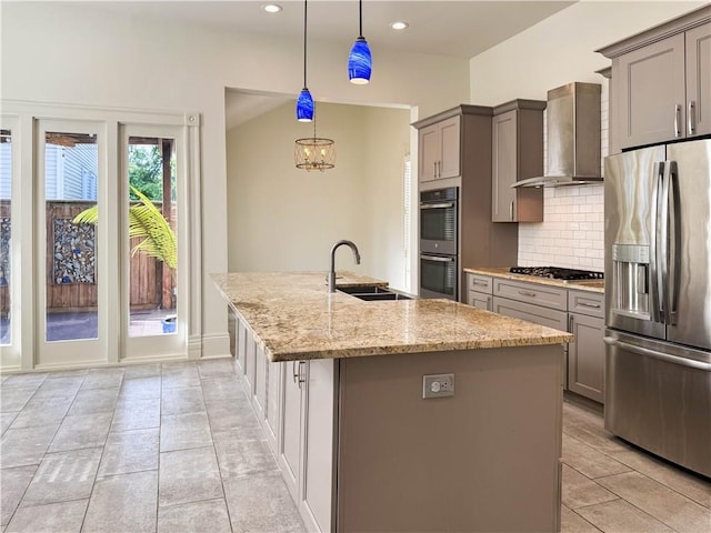 kitchen with light stone countertops, appliances with stainless steel finishes, wall chimney exhaust hood, sink, and pendant lighting