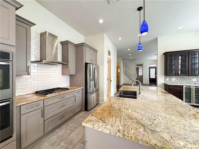 kitchen featuring wall chimney range hood, sink, appliances with stainless steel finishes, decorative light fixtures, and beverage cooler