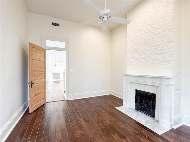 unfurnished living room featuring dark hardwood / wood-style floors, ceiling fan, and a stone fireplace