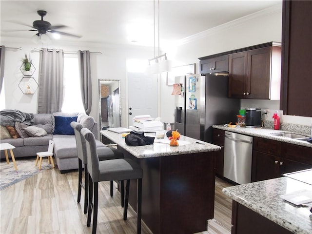 kitchen with a center island, light wood-type flooring, appliances with stainless steel finishes, light stone counters, and ceiling fan