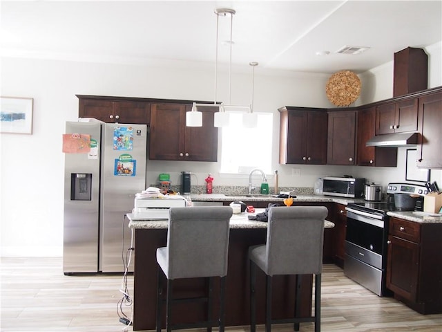 kitchen with light hardwood / wood-style flooring, pendant lighting, light stone counters, a center island, and appliances with stainless steel finishes