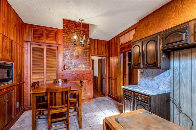 4102 Dauphine St, New Orleans, LA 70117 - kitchen with wood walls, light tile patterned floors, a textured ceiling, black microwave, and decorative light fixtures