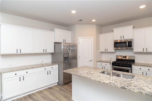 kitchen featuring white cabinets, backsplash, appliances with stainless steel finishes, and light hardwood / wood-style flooring