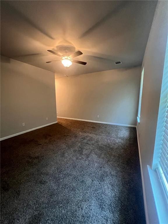 empty room featuring ceiling fan and dark colored carpet