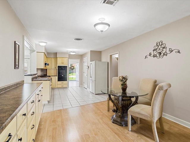 kitchen with light hardwood / wood-style floors, sink, cream cabinetry, black double oven, and white refrigerator