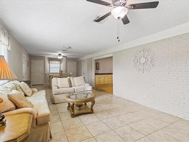 living room with a textured ceiling, light tile patterned floors, brick wall, and ceiling fan