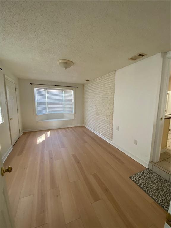 spare room with brick wall, a textured ceiling, and light hardwood / wood-style flooring