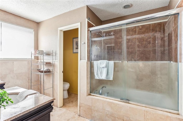 full bathroom with a textured ceiling, combined bath / shower with glass door, toilet, vanity, and tile walls