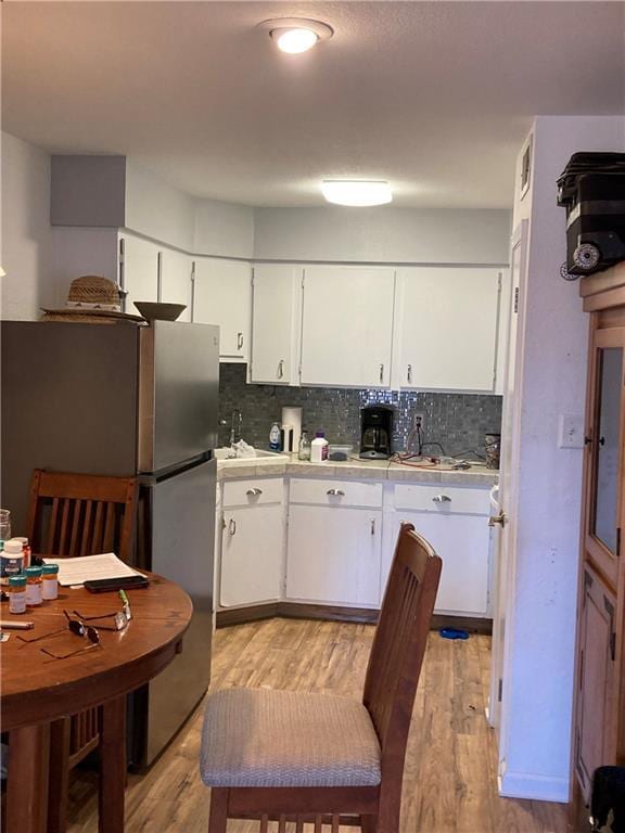 kitchen featuring white cabinetry, decorative backsplash, stainless steel refrigerator, and light hardwood / wood-style floors