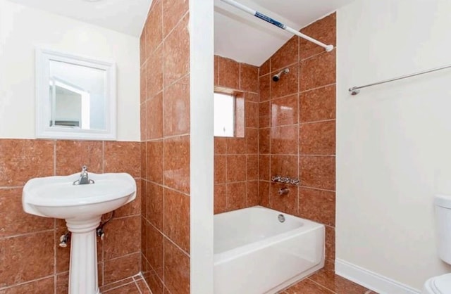 bathroom featuring tiled shower / bath, tile walls, toilet, and tile flooring