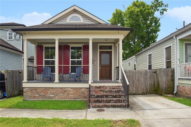 shotgun-style home featuring covered porch and fence