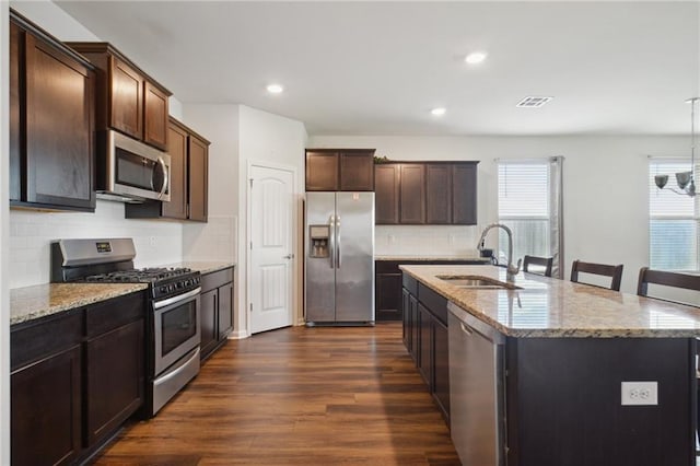 kitchen with appliances with stainless steel finishes, decorative light fixtures, sink, dark hardwood / wood-style flooring, and a kitchen island with sink