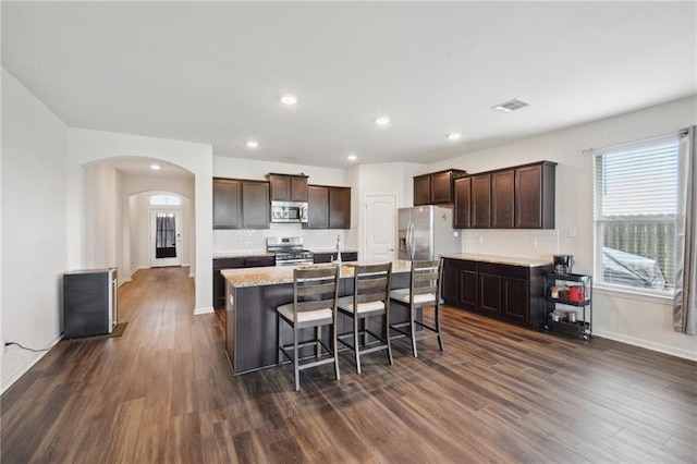 kitchen featuring dark brown cabinets, a center island with sink, dark hardwood / wood-style floors, and appliances with stainless steel finishes