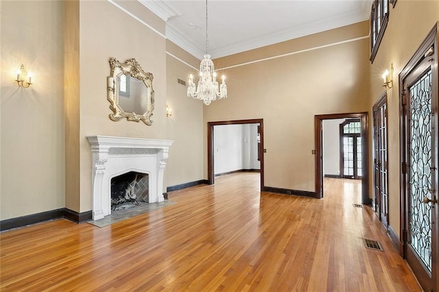 unfurnished living room featuring french doors, an inviting chandelier, light hardwood / wood-style floors, and ornamental molding