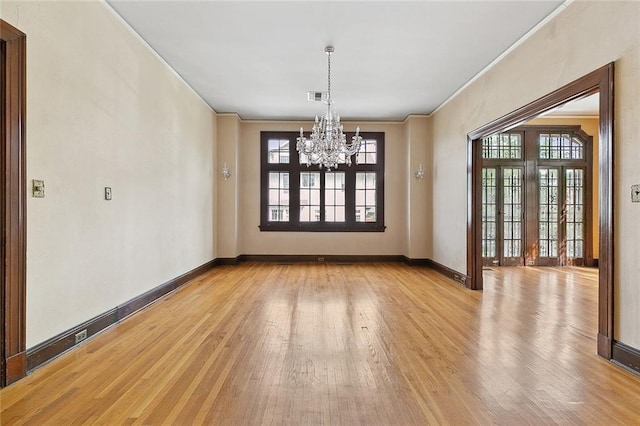 unfurnished dining area featuring an inviting chandelier, ornamental molding, light hardwood / wood-style flooring, and french doors