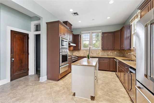 kitchen featuring appliances with stainless steel finishes, tasteful backsplash, sink, light tile patterned floors, and a center island