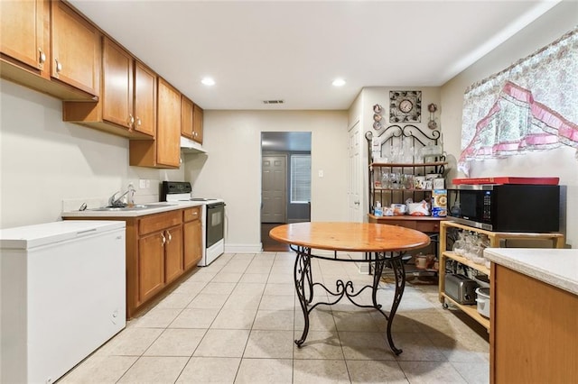 kitchen with brown cabinetry, stainless steel microwave, light countertops, white electric range, and fridge