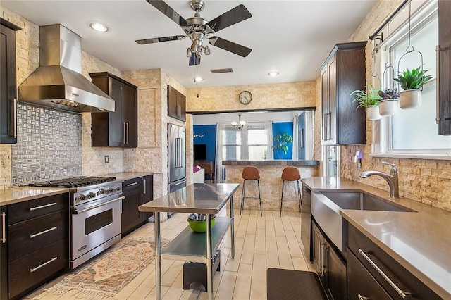 kitchen featuring high end appliances, pendant lighting, decorative backsplash, wall chimney exhaust hood, and sink