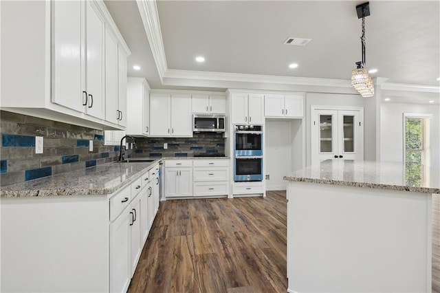 kitchen with pendant lighting, sink, stainless steel appliances, white cabinets, and a kitchen island