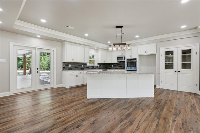 kitchen featuring french doors, white cabinetry, decorative light fixtures, an island with sink, and light stone countertops