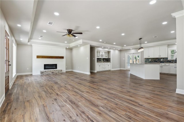 unfurnished living room featuring dark hardwood / wood-style flooring, a brick fireplace, a tray ceiling, and plenty of natural light