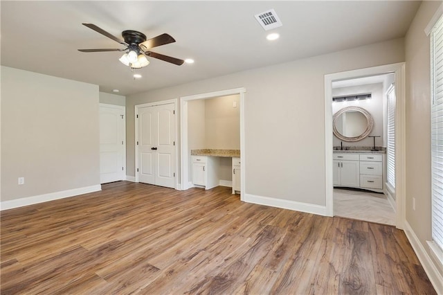 unfurnished bedroom with sink, ensuite bath, built in desk, ceiling fan, and light hardwood / wood-style floors