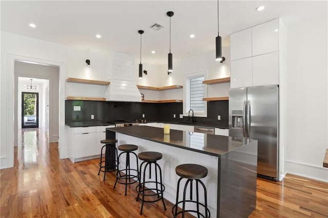 kitchen with a center island, decorative backsplash, appliances with stainless steel finishes, light hardwood / wood-style floors, and white cabinetry