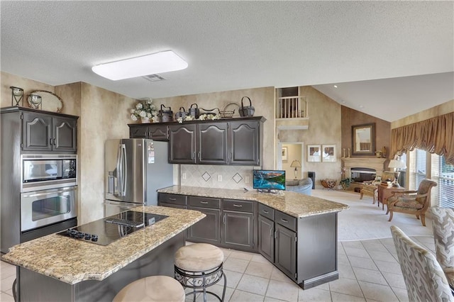 kitchen featuring lofted ceiling, stainless steel appliances, dark brown cabinetry, a kitchen bar, and light tile patterned flooring