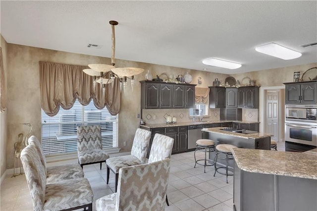 kitchen featuring light tile patterned floors, appliances with stainless steel finishes, hanging light fixtures, backsplash, and a kitchen island