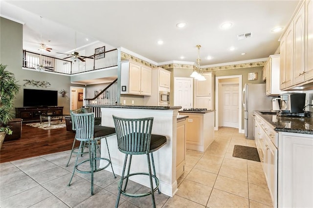 kitchen with light tile patterned floors, dark stone countertops, stainless steel appliances, a center island, and decorative light fixtures