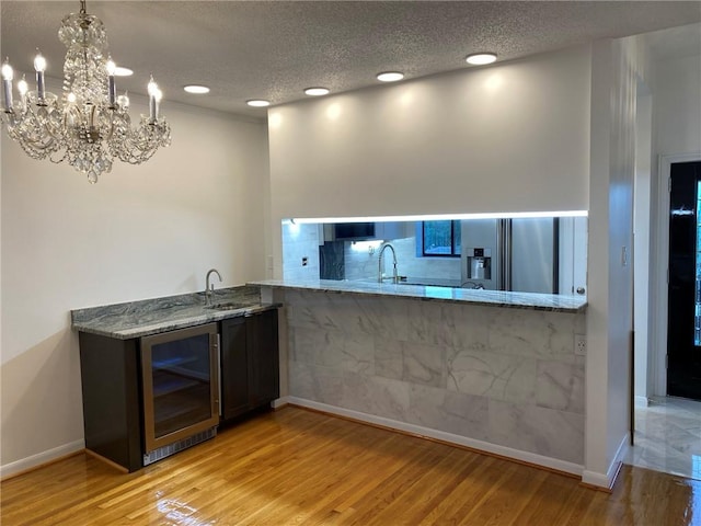 kitchen with wine cooler, light hardwood / wood-style flooring, stainless steel refrigerator with ice dispenser, an inviting chandelier, and light stone counters