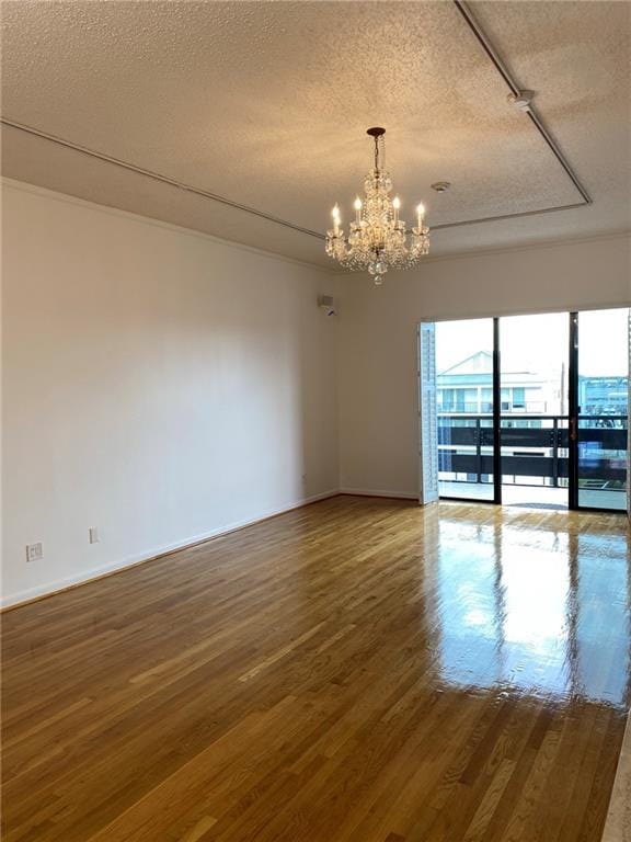 empty room with a notable chandelier, track lighting, a textured ceiling, and dark hardwood / wood-style floors