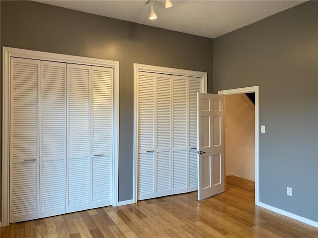 unfurnished bedroom featuring two closets, light hardwood / wood-style flooring, and a textured ceiling