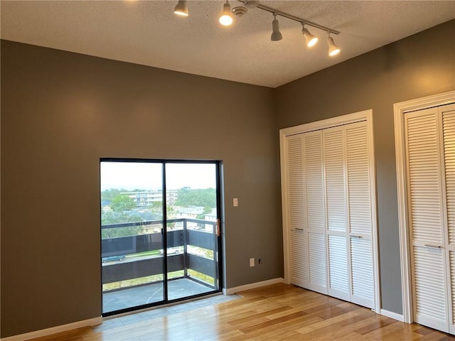 unfurnished bedroom featuring two closets, track lighting, light wood-type flooring, and access to outside