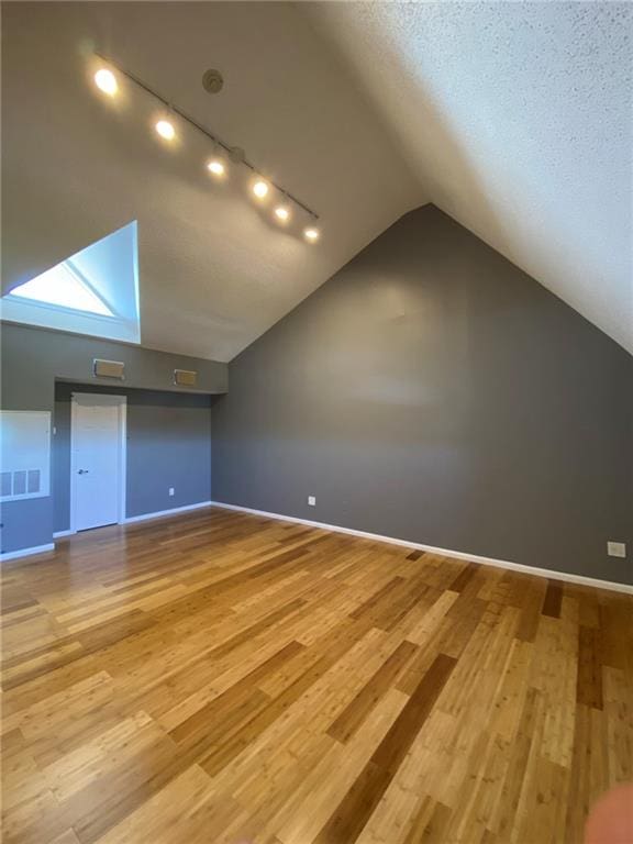 additional living space with vaulted ceiling, light hardwood / wood-style flooring, and a textured ceiling