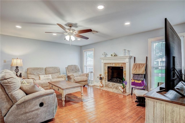 living room with a high end fireplace, hardwood / wood-style floors, and ceiling fan