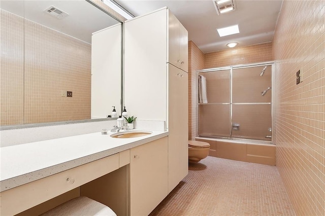 full bathroom featuring shower / bath combination with glass door, tile walls, vanity, tile patterned floors, and toilet