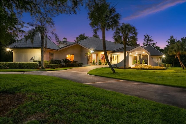 single story home with curved driveway, a chimney, a front lawn, and stucco siding