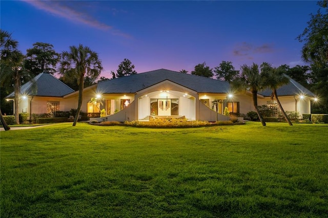 front of property at dusk featuring stucco siding and a yard