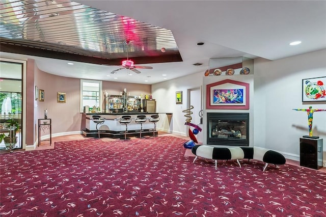 carpeted living area with a glass covered fireplace, recessed lighting, a bar, and baseboards