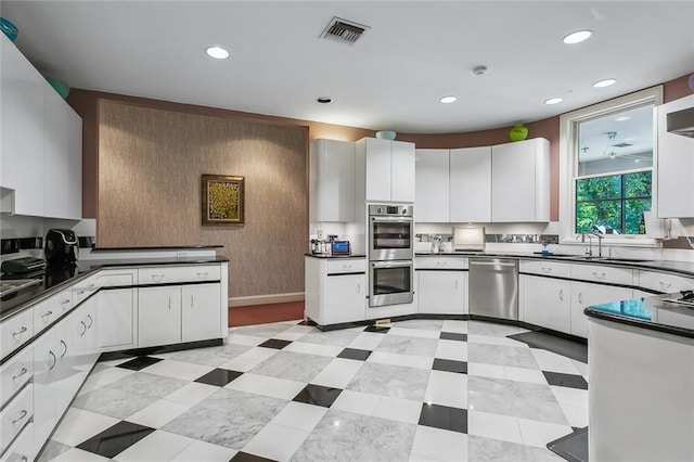 kitchen featuring dark countertops, visible vents, stainless steel appliances, white cabinetry, and a sink