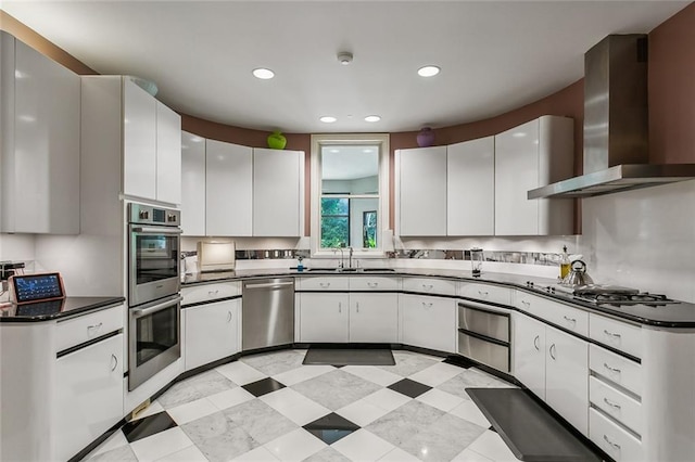 kitchen with a sink, stainless steel appliances, dark countertops, and wall chimney exhaust hood