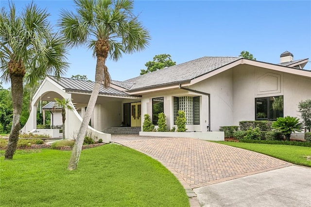 rear view of house with stucco siding, a lawn, decorative driveway, and a standing seam roof