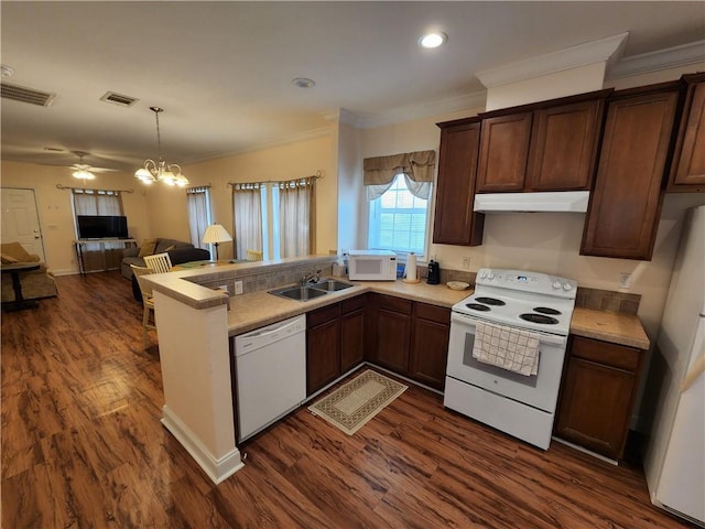 kitchen featuring sink, white appliances, dark wood-type flooring, hanging light fixtures, and kitchen peninsula