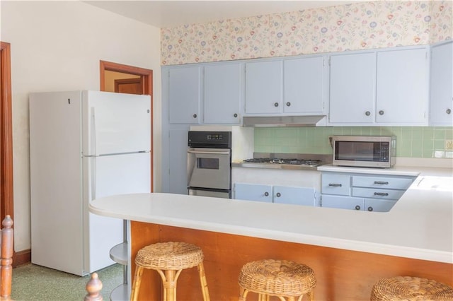 kitchen with stainless steel appliances, a kitchen bar, kitchen peninsula, and decorative backsplash