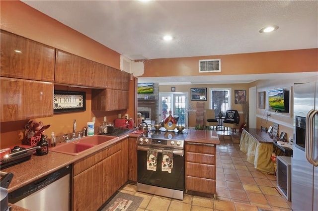 kitchen featuring light tile patterned flooring, sink, appliances with stainless steel finishes, kitchen peninsula, and a fireplace