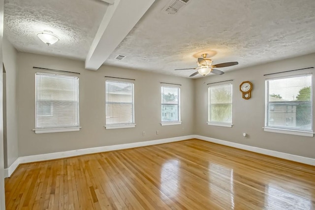 empty room with a wealth of natural light, beamed ceiling, light hardwood / wood-style floors, and a textured ceiling