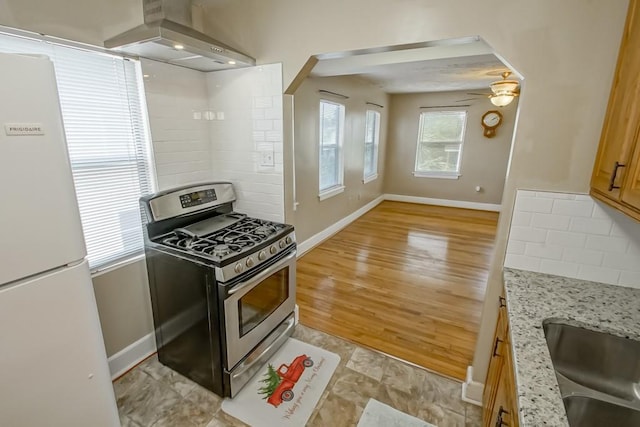 kitchen featuring light wood-type flooring, light stone counters, stainless steel gas range, island range hood, and white refrigerator